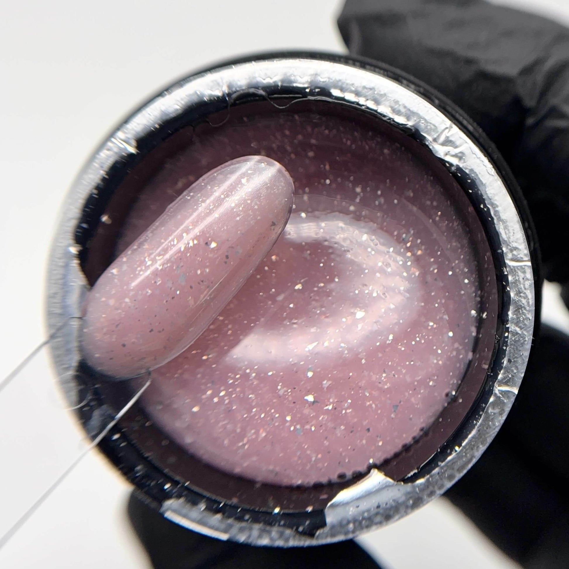 Pink glittery gel in a container with a gloved hand holding it.