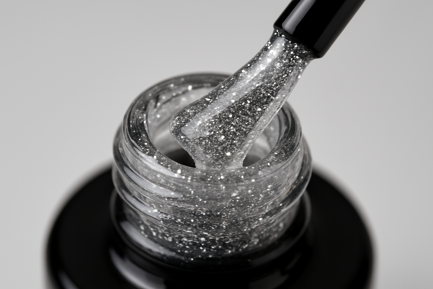gel bottle opened, black brush is touching the bottle neck, clear gel with very fine silver glitter is on the brush