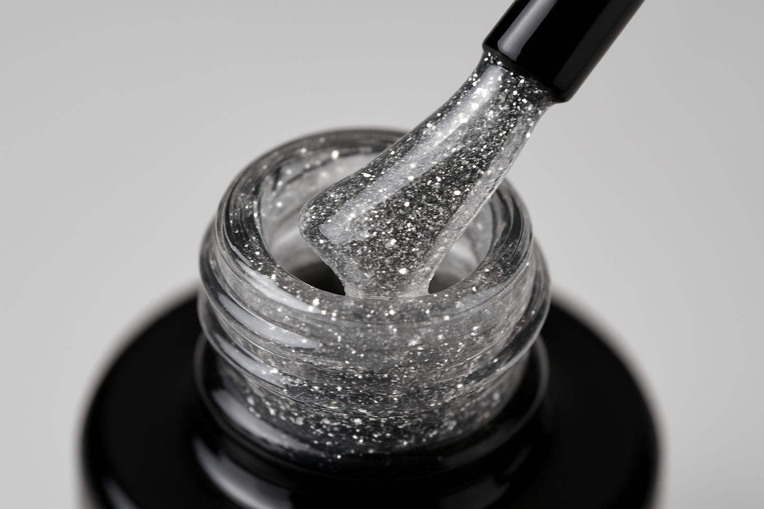 gel bottle opened, black brush is touching the bottle neck, clear gel with very fine silver glitter is on the brush