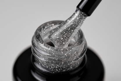 gel bottle opened, black brush is touching the bottle neck, clear gel with very fine silver glitter is on the brush